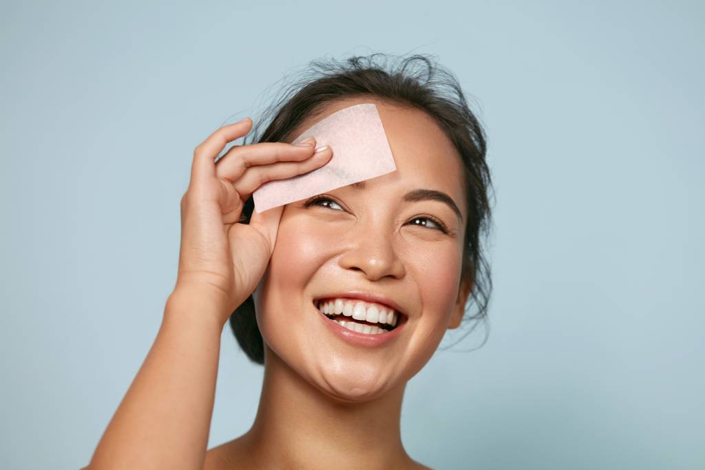 Smiling woman blotting oily t-zone with paper