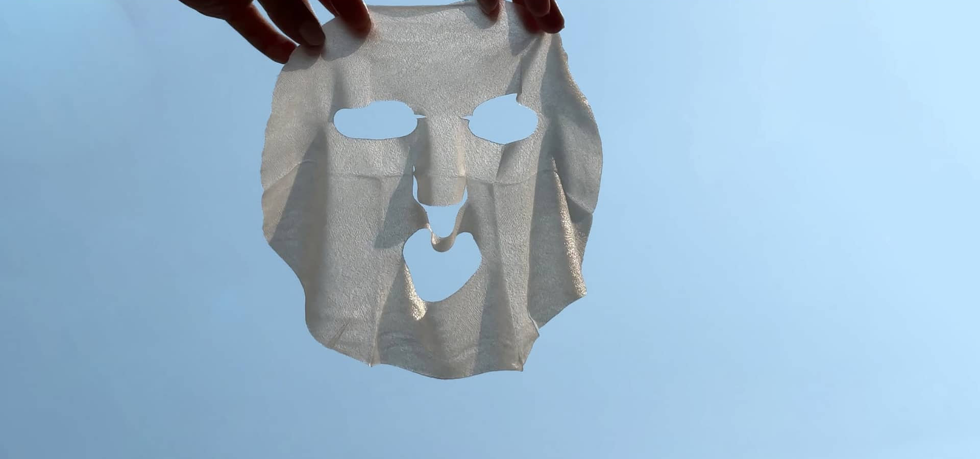 hands holding a sheet mask against the bright blue sky
