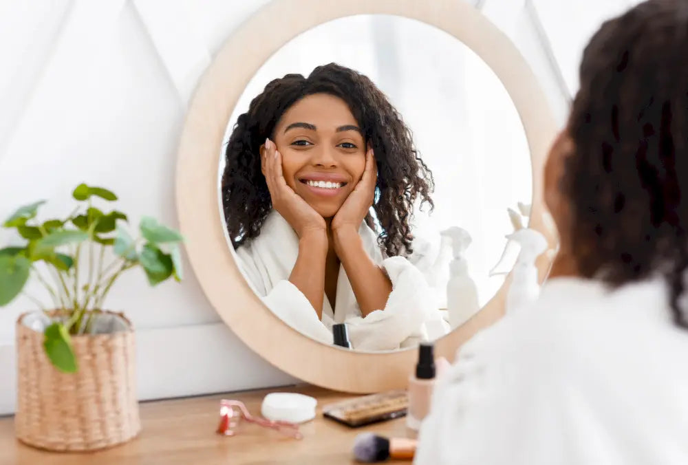 Smiling woman in bathrobe practicing morning self-care routine in mirror