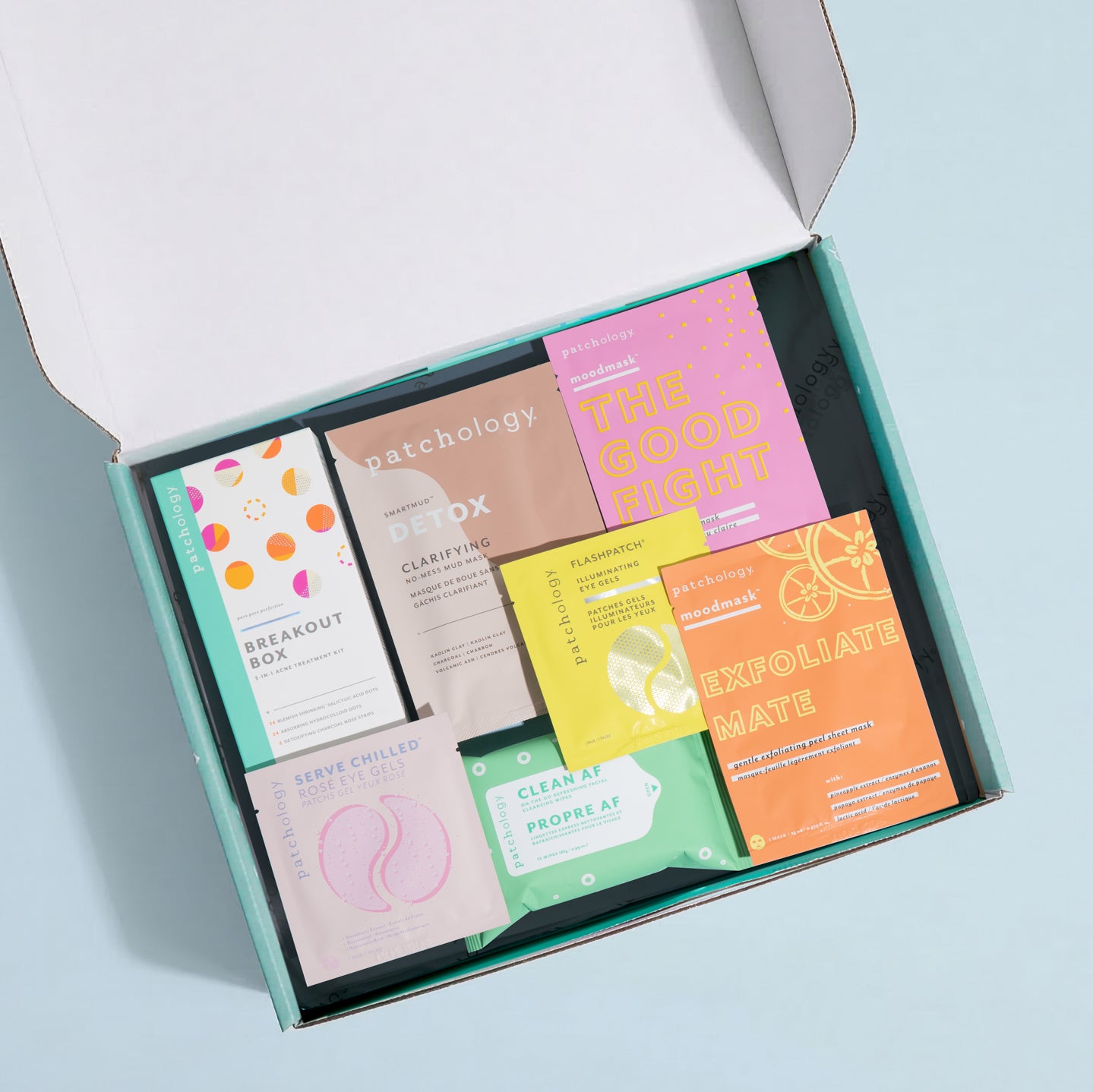 Open box containing various skincare product packages with colorful labels on a light blue background.