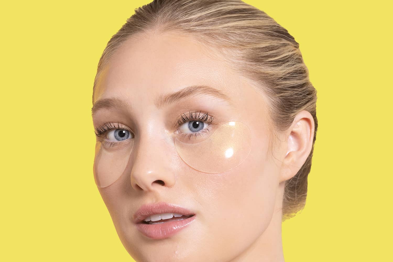 Woman with under-eye Illumin ate eye patches on a yellow background
