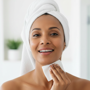 Woman with a towel wrapped around her head, using a white cloth to wipe her face.