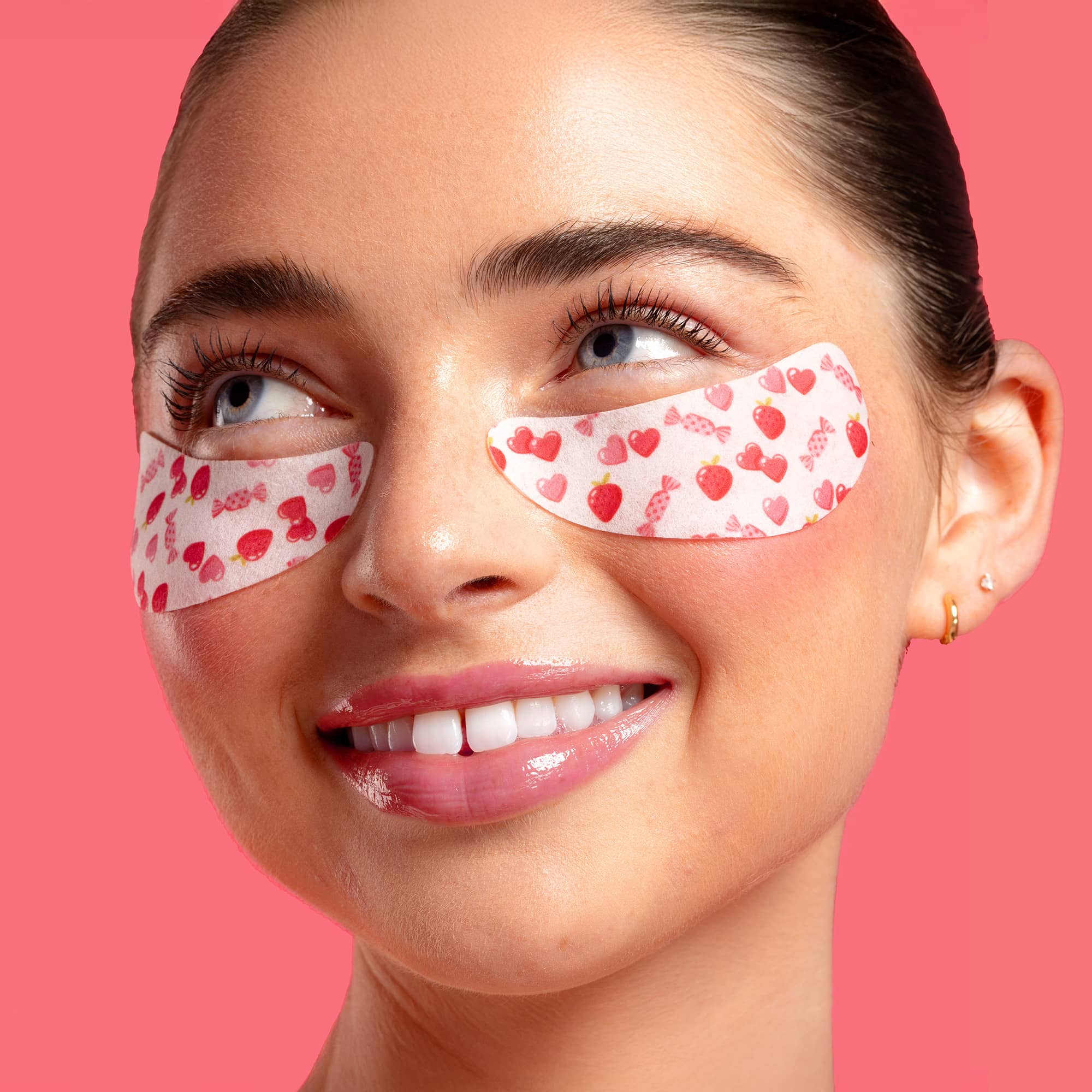 Woman wearing red heart-themed eye patches on a pink background