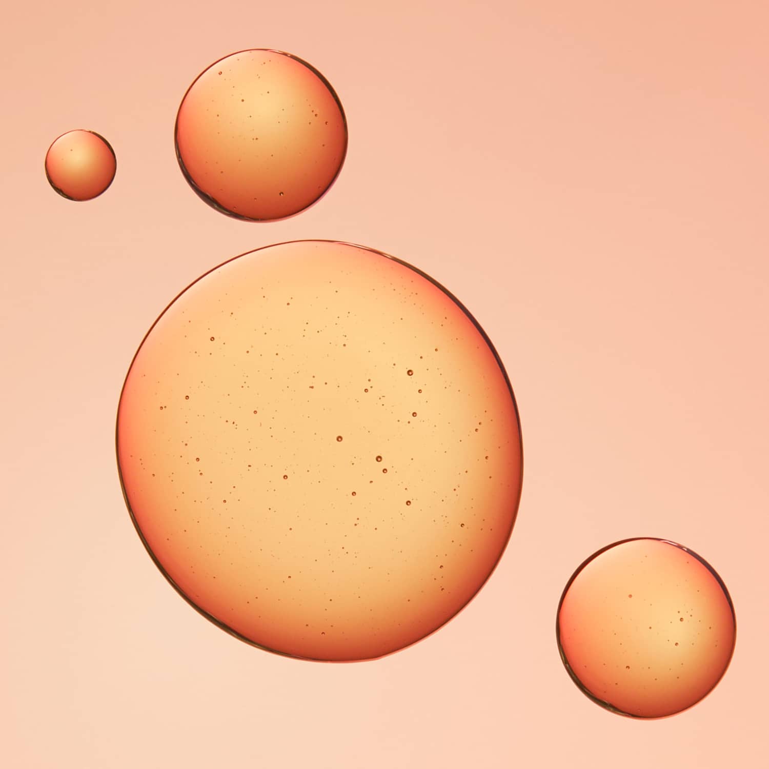 Three translucent orange spheres of varying sizes floating on a soft peach-pink background of glow potion serum