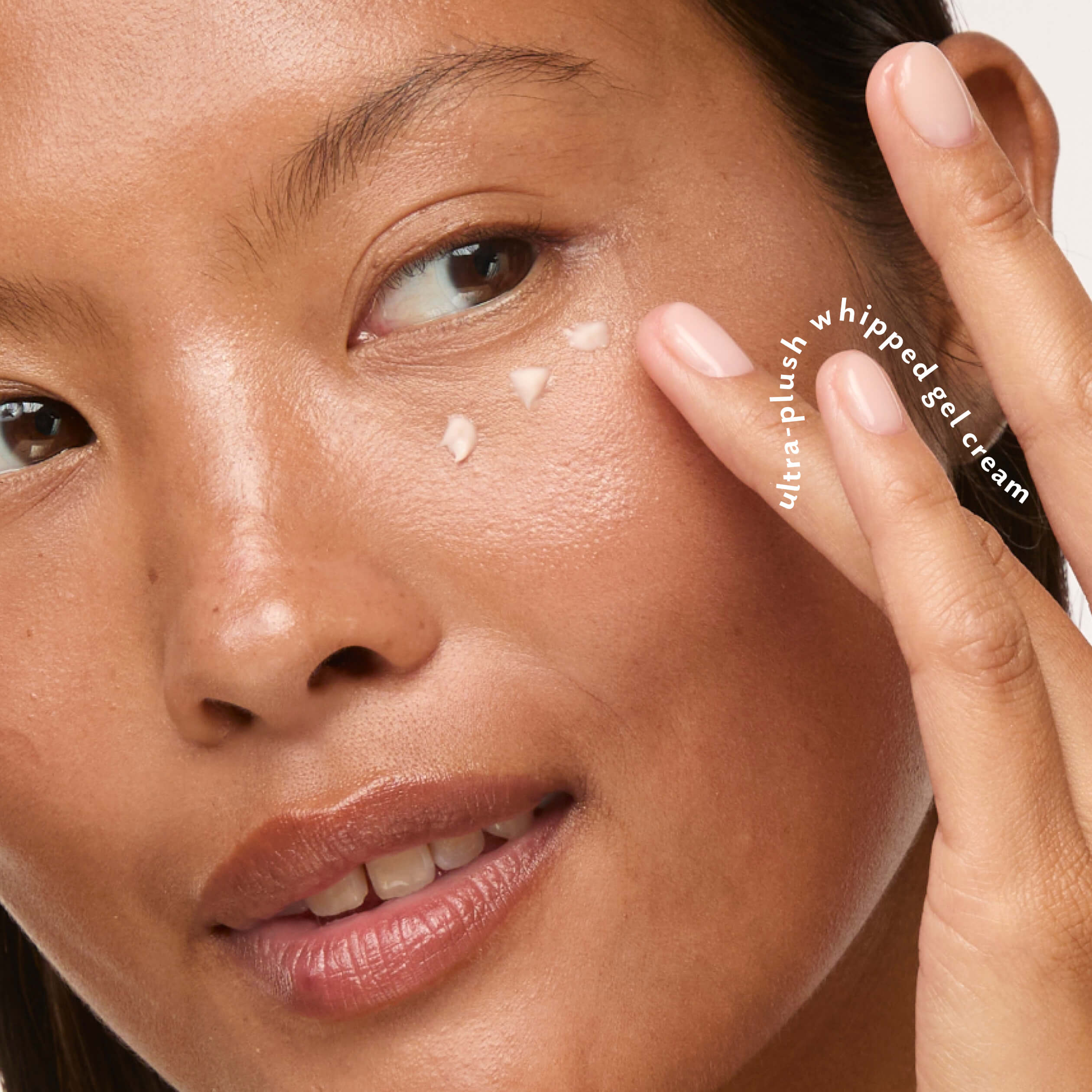 Close-up of a woman applying cream-colored whipped gel cream to her cheek, with her fingers touching her face. White text on the right reads 'ultra-plush whipped gel cream'.