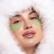Woman wearing green eye patches with a white fuzzy hood