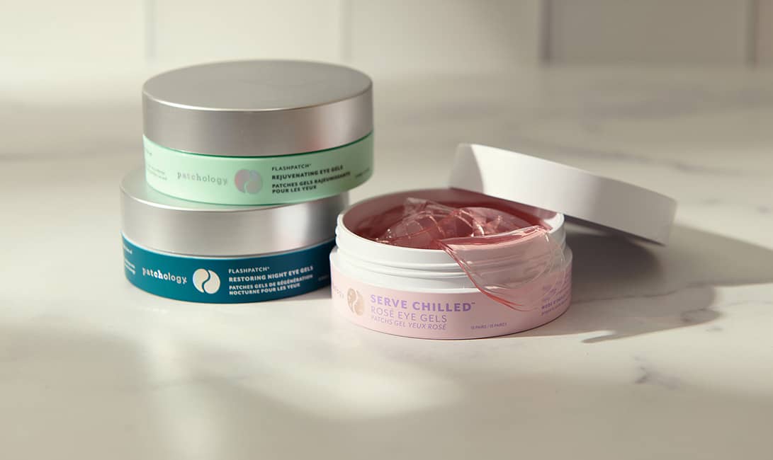 Stacked Patchology eye gel jars featuring an open container of pink Rosé Eye Gels on a white marble surface.