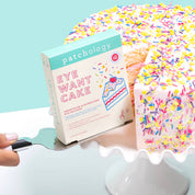 Patchology 'Eye Want Cake' eye patch box with a cake-shaped product on a stand against a light blue background.