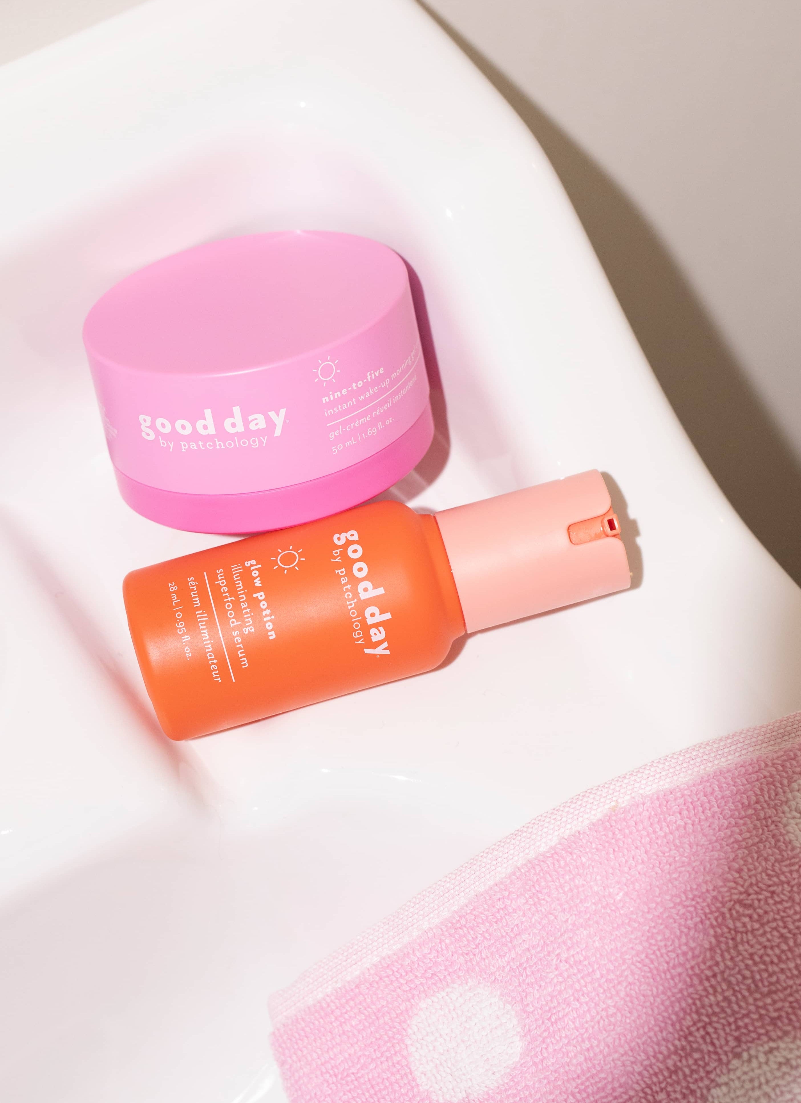 Skincare face time set featuring a pink cream jar and an orange spray bottle with a pink cap, styled on a white ceramic surface with a pink towel in the corner.