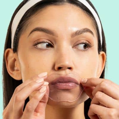 Woman applying a hydrating lip gel to her face against a light blue background