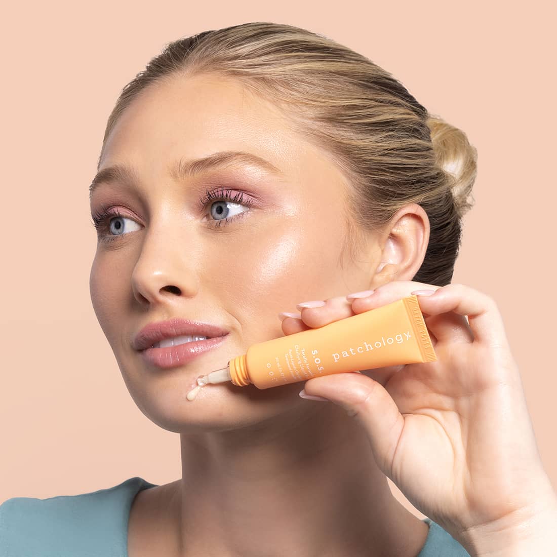Woman applying skincare SOS product to her face with a beige background