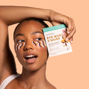 Woman with eye masks holding a skincare product against a peach background