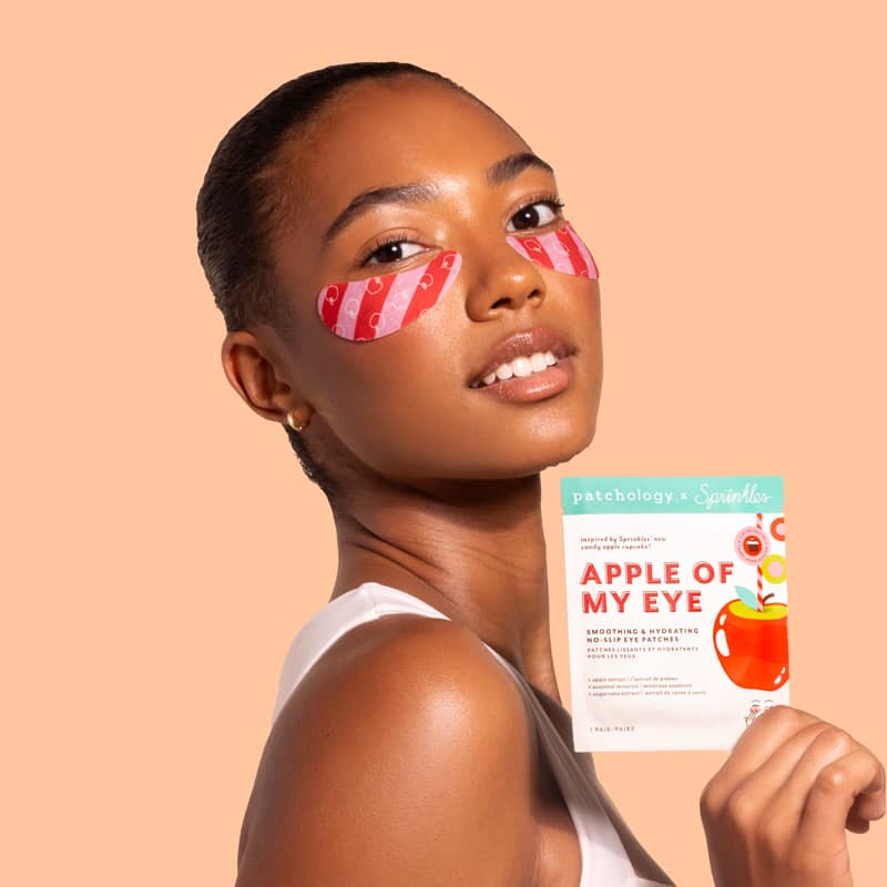 Woman wearing exclusive Sprinkles apple of my eye under-eye patches with a product packaging on a beige background