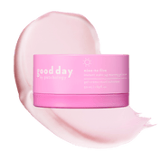 A pink cosmetic jar labeled 'good day' nine-to-five placed over a large pale pink cream smear on a black background.
