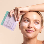Woman wearing soothing skin remedy eye patches on a light tan background