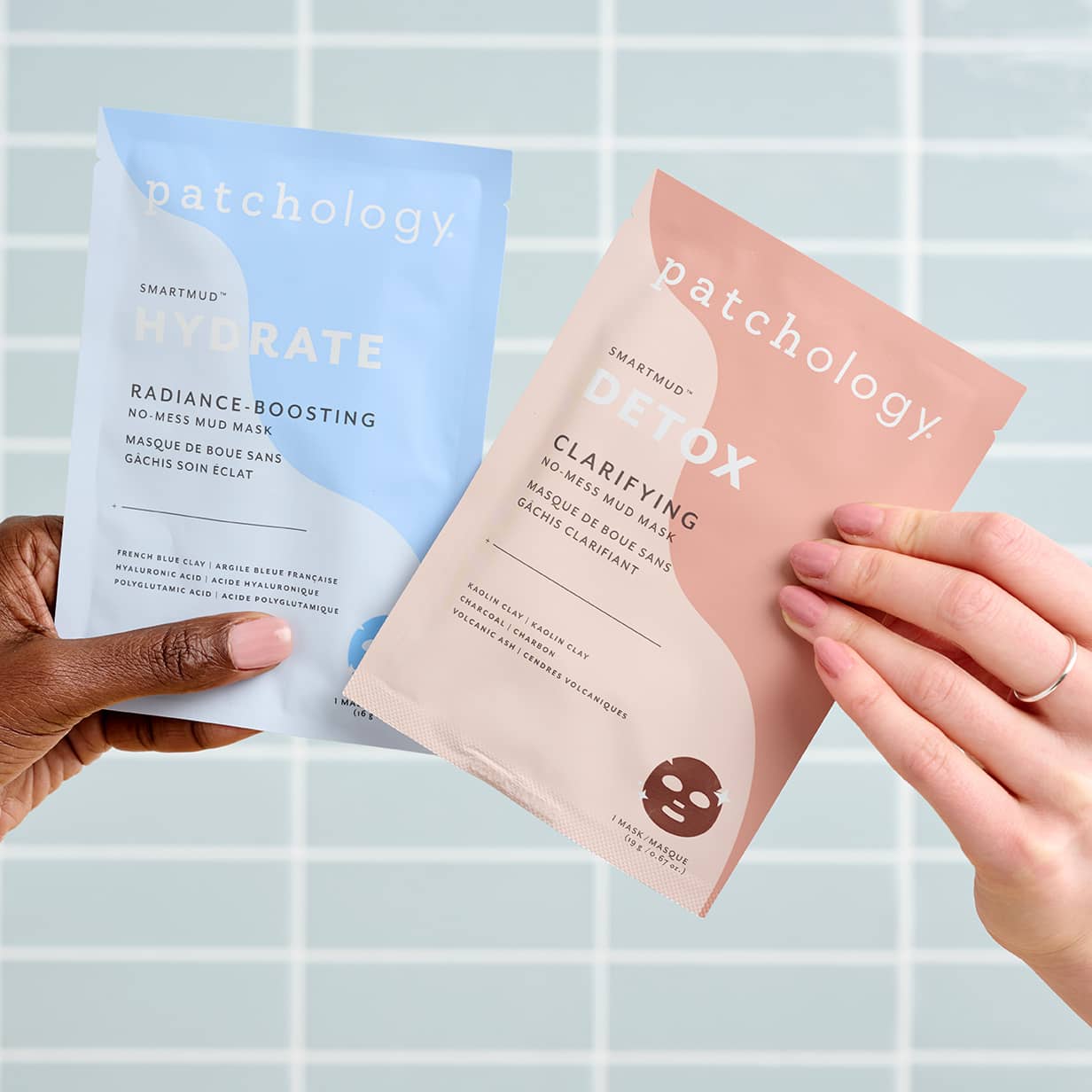 Hands holding Patchology SmartMud Hydrate and Detox mud mask sachets, blue and pink skincare packets against tiled background