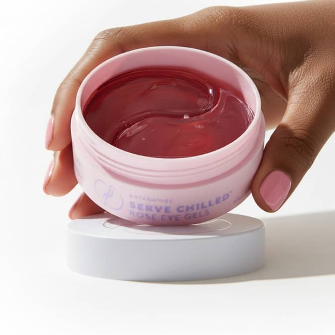 Hand holding a hydrating jar of under-eye patches rose on a white background