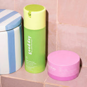 Two hydrating skincare products arranged on a pink tiled surface: a blue-and-white striped jar on the left, a green and yellow bottle in the center, and a pink jar on the right.